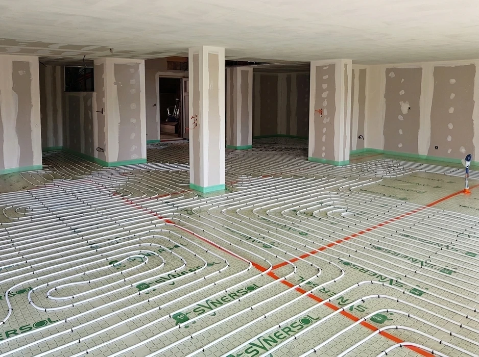 Gros plan ou vue d'ensemble d'un sol résidentiel avec système de plancher chauffant visible lors de son installation ou en fonctionnement - montrant les tubes de circulation d'eau chaude intégrés dans la dalle ou le revêtement de sol dans un intérieur domestique moderne et confortable.