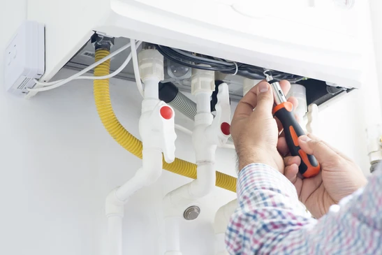 Technicien chauffagiste en uniforme professionnel effectuant un dépannage urgent sur une chaudière murale domestique, en train de vérifier les connexions hydrauliques ou le panneau de contrôle avec un multimètre ou un appareil de diagnostic, dans un intérieur résidentiel réaliste montrant la relation de confiance avec le client ou son intervention focalisée sur l'équipement. La scène doit mettre l'accent sur l'expertise technique et la professionnalité du dépannage d'urgence.